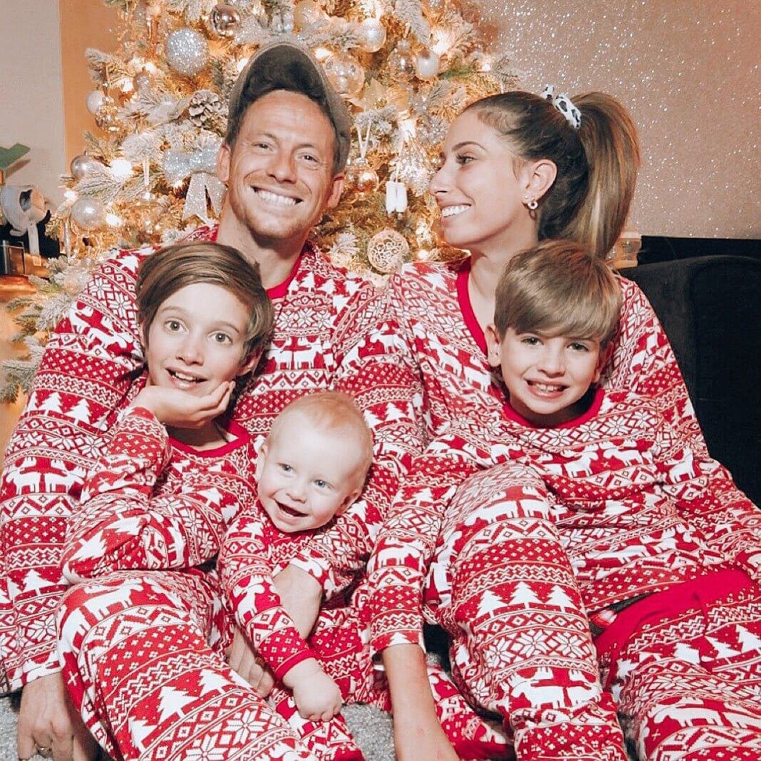 Family of five with three kids smiling together in front of a decorated Christmas tree, all dressed in matching long-sleeve red and white Fair Isle holiday pajama sets.