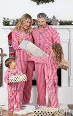 Family of four standing together in front of a glowing Christmas tree with present boxes, wearing matching red and white candy cane striped pajamas.