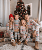 Family sitting by a Christmas tree in matching grey pajamas patterned with red reindeer and green snowflakes.