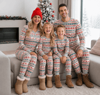 Family sitting on a sofa in grey Fair Isle Christmas pajamas and boots, with a snowy tree behind them.