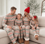 Parents and two children smiling together on a cream sofa in grey, red and green Fair Isle Christmas pajamas.