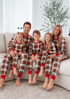 Parents and three children sitting on a cream sofa in matching red, white and black tartan Christmas pajamas.