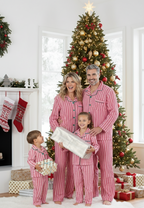 Parents and two children holding wrapped Christmas gifts by a decorated fireplace in matching red and white candy cane striped pajamas.