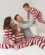 Dad lifting his son above a bed as the family plays in red and white striped pajamas with grey trim.