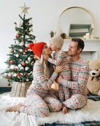 Mother kissing her child beside a Christmas tree as dad watches, all wearing matching grey Fair Isle pajamas.