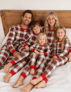 Family cuddling on a bed in matching red, white and black tartan Christmas pajamas with red neckline and cuffs.