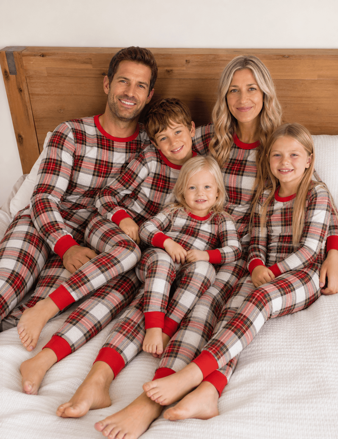 Family cuddling on a bed in matching red, white and black tartan Christmas pajamas with red neckline and cuffs.