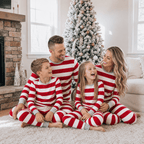 Family sitting on a rug by a stone fireplace in red and white wide-striped Christmas pajamas with grey trim.