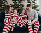 Family sitting on a blue sofa in red and white striped Christmas pajamas, with dad in a grey Henley.