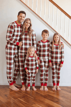 Family standing beside a staircase in red, white and black tartan Christmas pajamas with red cuffs.