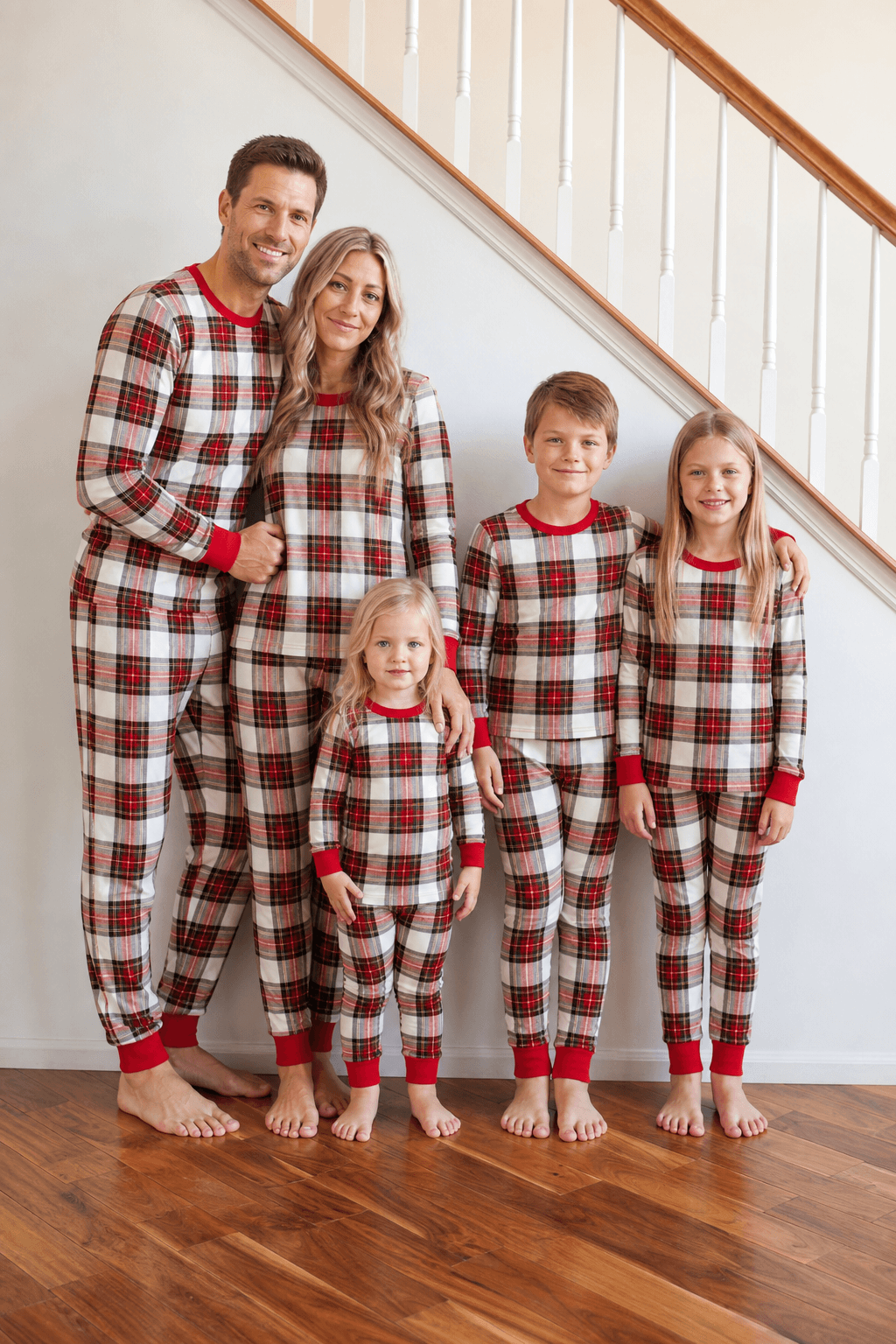 Family standing beside a staircase in red, white and black tartan Christmas pajamas with red cuffs.
