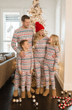 Family standing near a lit Christmas tree in grey Fair Isle pajamas, with ornaments scattered on the floor.