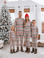 Family standing beside a snowy Christmas tree in matching grey Fair Isle pajamas and brown winter boots.