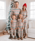 Family posing by a snowy Christmas tree in grey Fair Isle pajamas with red reindeer and green snowflakes.