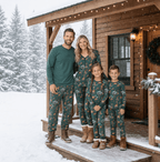 Family standing on a snowy cabin porch in forest green animal-print Christmas pajamas and brown boots.