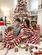 Family opening presents by a Christmas tree in red and white striped pajamas, with dad in a grey Henley.