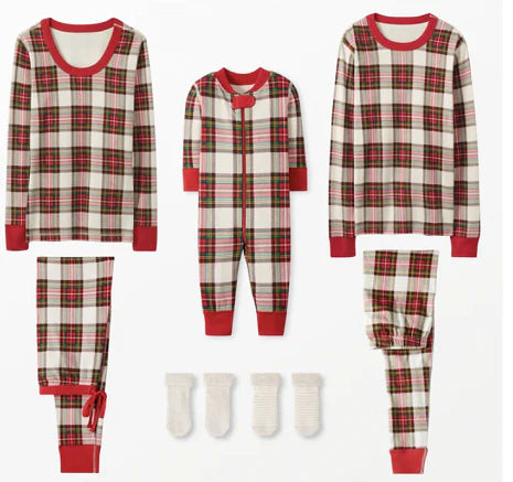 Father and curly-haired son sitting on wooden stools outdoors looking at each other, wearing matching cream, red, and green plaid Christmas pajamas.