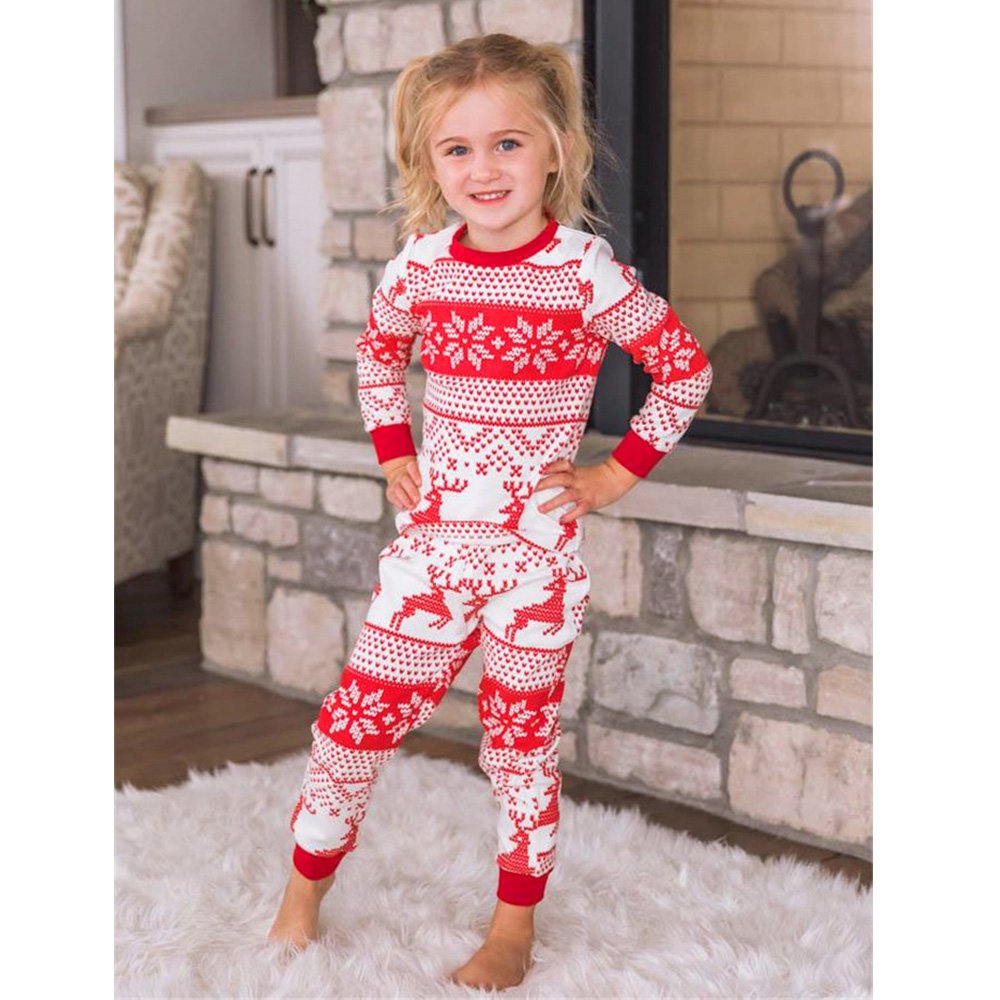 Girl standing with hands on hips in red and white reindeer Christmas pajamas beside a stone fireplace.