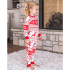 Side profile view of a happy young girl standing by a stone fireplace, demonstrating the side fit of the red and white Fair Isle reindeer matching Christmas pajamas.