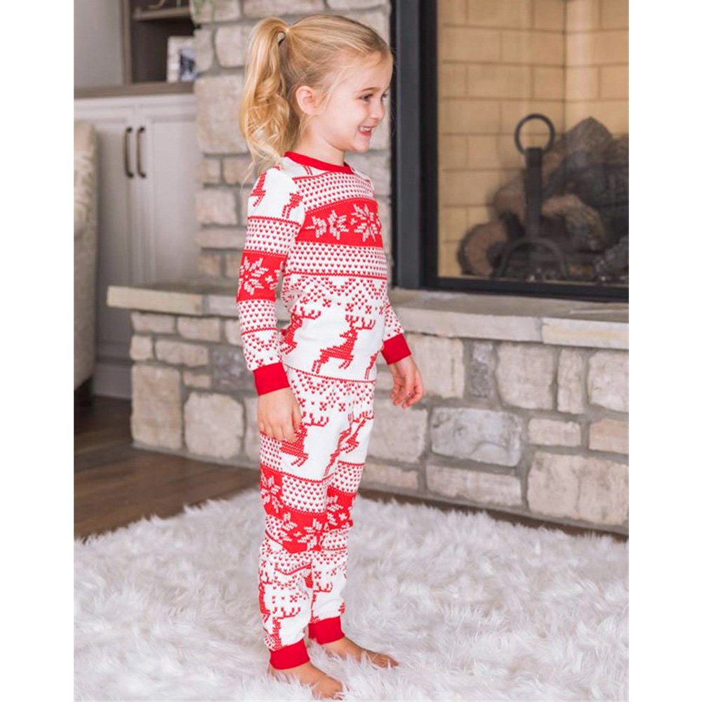 Side profile view of a happy young girl standing by a stone fireplace, demonstrating the side fit of the red and white Fair Isle reindeer matching Christmas pajamas.
