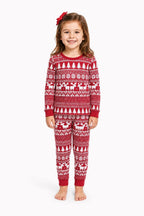 Girl wearing red Christmas pajamas with white tree and reindeer patterns, red cuffs and a red hair bow.