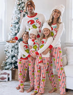 Family wearing white Grinch pajama tops and striped pants beside a decorated Christmas tree.