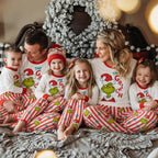 Family wearing matching Grinch Christmas pajamas with white tops and striped pants in a festive living room.