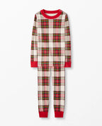 Young boy walking ahead on an outdoor path with his family following behind, all wearing matching cream and red plaid holiday pajama sets.