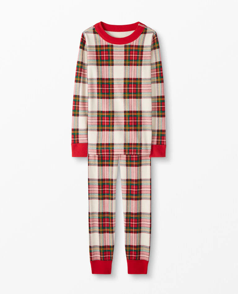 Young boy walking ahead on an outdoor path with his family following behind, all wearing matching cream and red plaid holiday pajama sets.