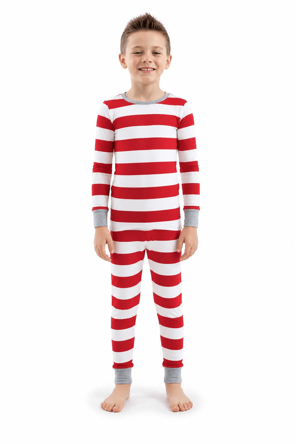 Boy standing in Christmas pajamas with wide red and white stripes, long sleeves and grey cuffs.