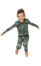 Boy jumping playfully in dark green safari Christmas pajamas demonstrating comfortable stretch fabric.