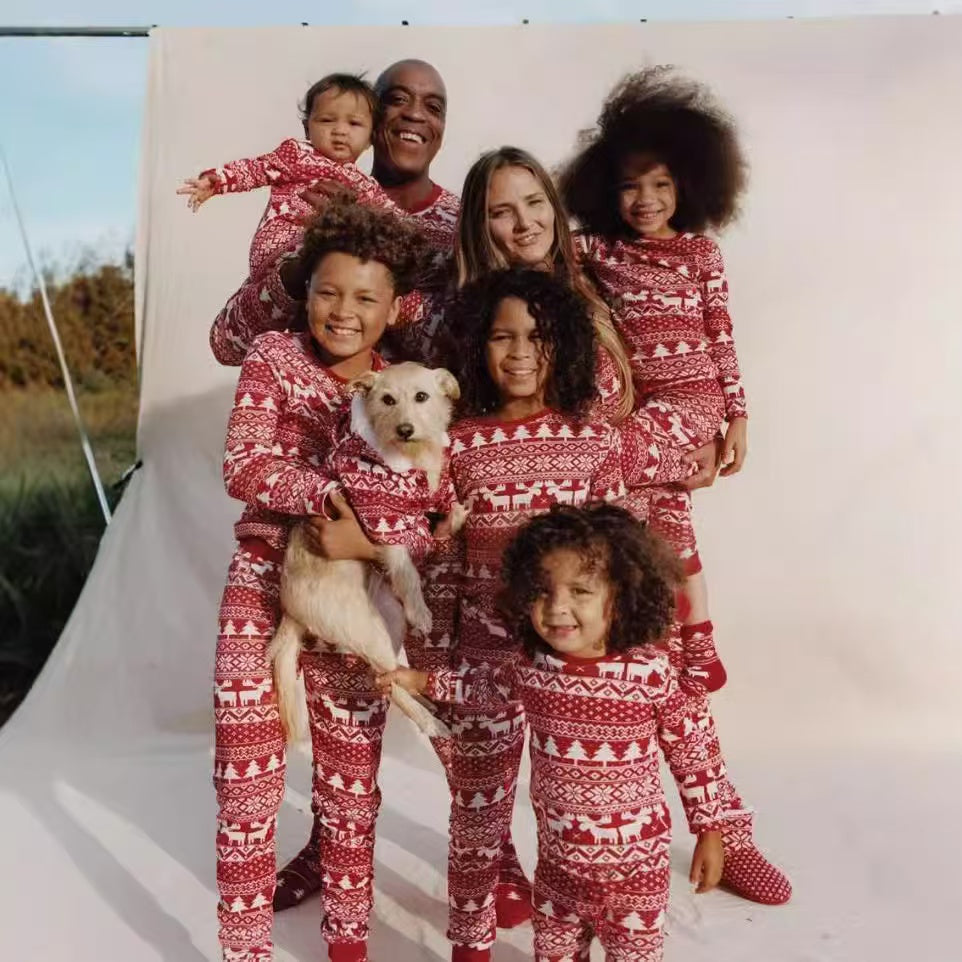 Large family posing with a dog in matching red and white Fair Isle pajamas with reindeer and Christmas trees.