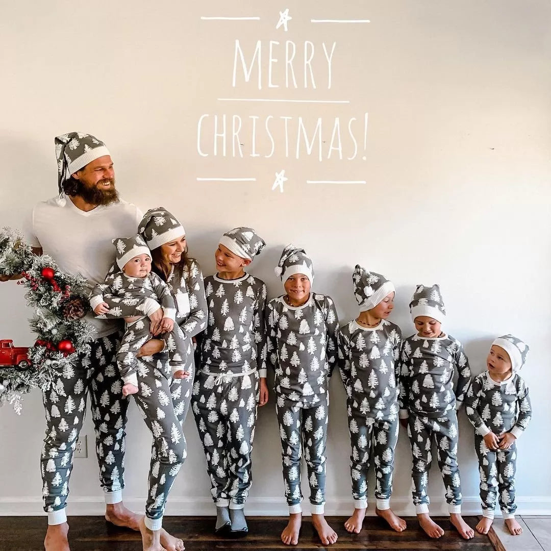 Large family in grey tree-print pajamas and hats beneath Merry Christmas lettering, with dad in a white T-shirt.
