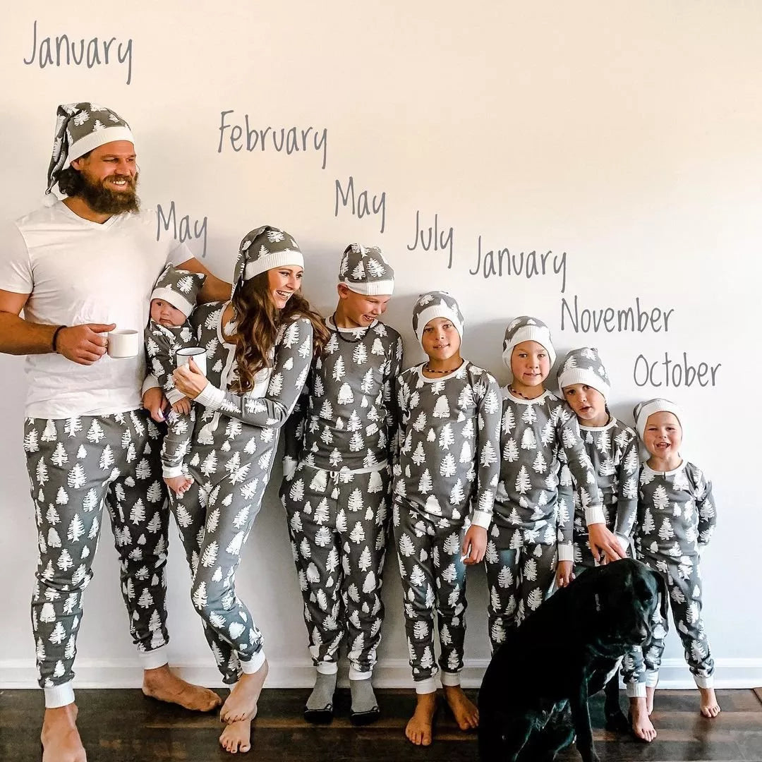 Large family with a black dog in grey tree-print pajamas and hats, standing beneath handwritten month names.