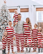 Large family with five kids smiling in front of a frosted Christmas tree, all wearing matching red and white striped holiday pajamas with dad in a grey henley top.