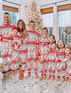 Large family standing together in red and white reindeer Christmas pajamas beside a snowy Christmas tree.