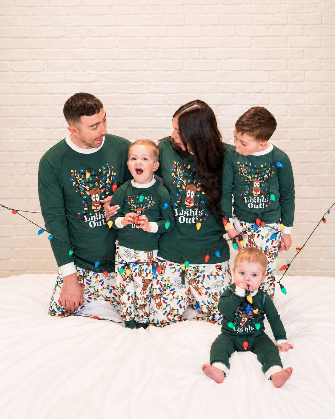 Family wearing green Lights Out reindeer Christmas pajamas with matching printed pants and a baby romper
