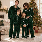 Family wearing matching green velvet Christmas pajamas and a girls' nightgown beside a Christmas tree