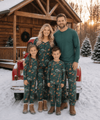 Family posing by a red truck and snowy wooden cabin in green animal-print Christmas pajamas and boots.