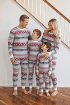 Parents and two boys beside a staircase in light grey Fair Isle Christmas pajamas with red reindeer and green trees.