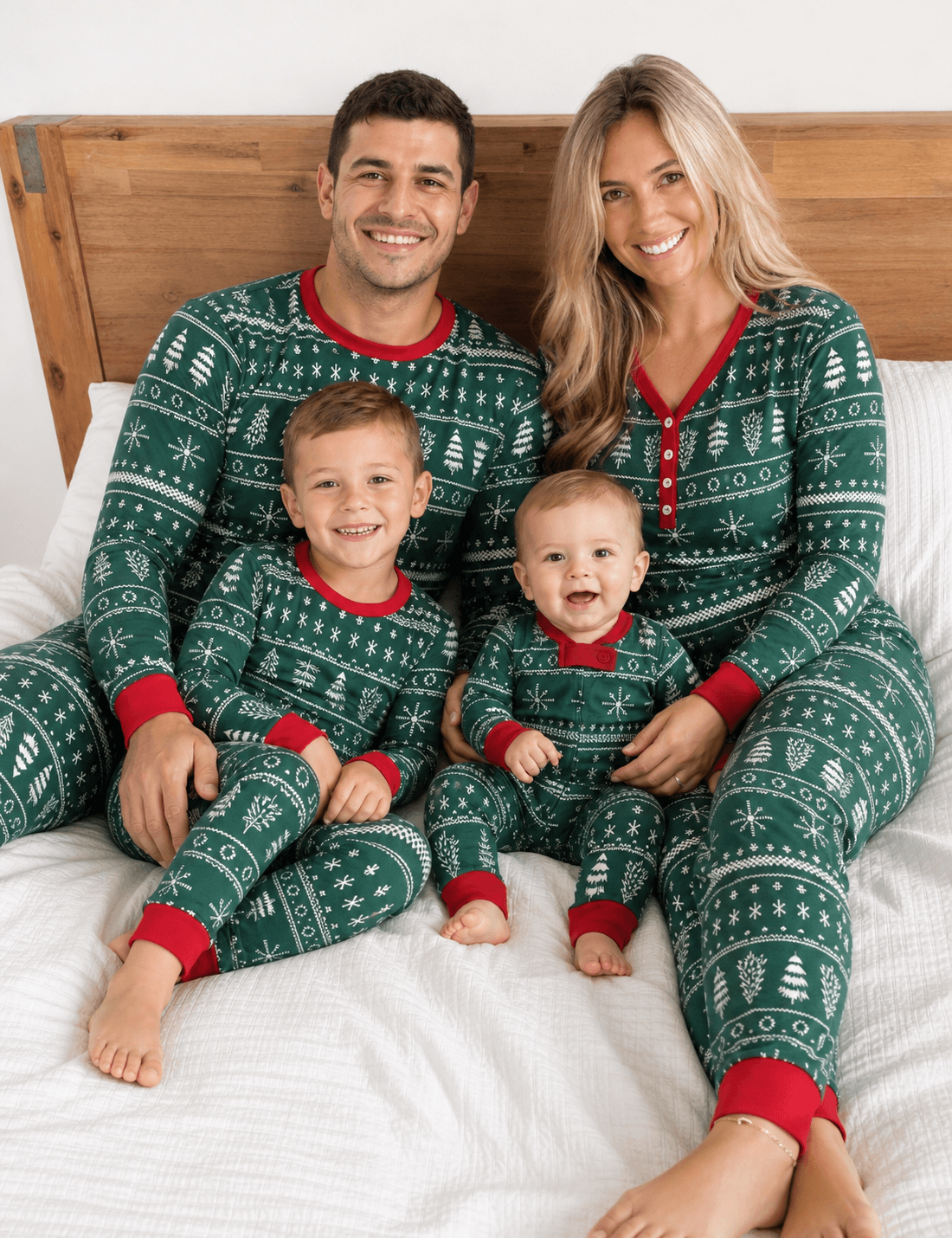 Parents, a boy and a baby sitting on a bed in green Christmas pajamas with white Fair Isle patterns and red trim.