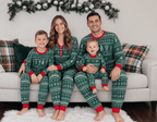Parents, a boy and a baby on a sofa beneath a garland in green Christmas pajamas with white motifs and red trim.