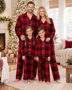 Family of four in matching red and black plaid pajamas beside a decorated Christmas tree.