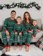 Family seated on a sofa under a holiday garland in green tree-and-snowflake pajamas with red neckline and cuffs.