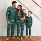 Family standing beside a staircase in matching green Christmas pajamas with white tree and snowflake motifs.