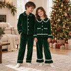 Children wearing matching green velvet Christmas pajamas beside wrapped gifts