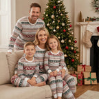 Parents and two children sitting on a beige couch in front of a festive Christmas tree, wearing matching grey and red Fair Isle holiday sleepwear sets.