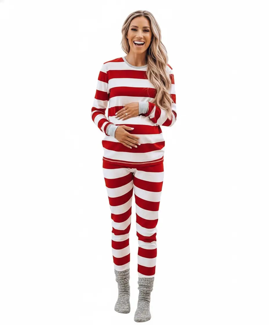 Smiling pregnant woman holding her baby bump on a white background wearing a two-piece red and white striped Christmas pajama set with grey cuffs.