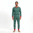 Man modeling forest green Christmas pajamas with white tree and snowflake rows, a red crewneck and red cuffs.