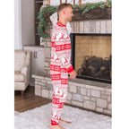 Side view of a man in red and white Fair Isle reindeer Christmas pajamas standing beside a stone fireplace.